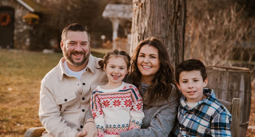 A smiling family with 2 children outside on the grass.